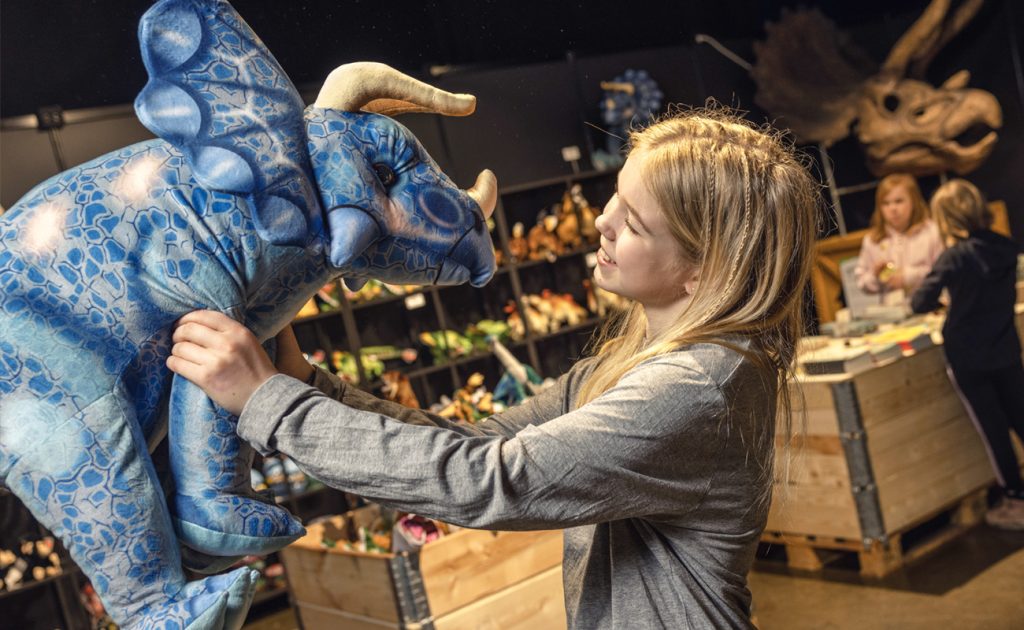 Tyttö pitää kädessään isoa Dinosaurus-pehmoeläintä.