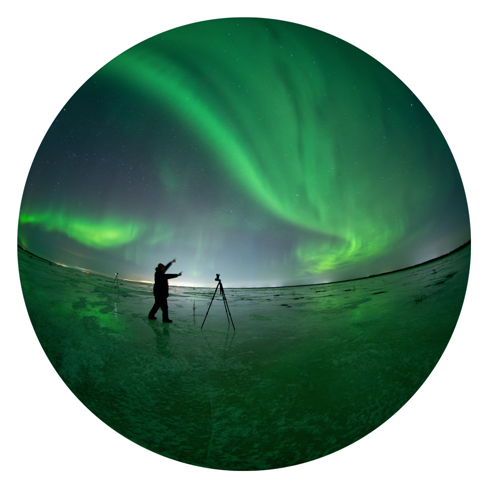 Laajakuva, jossa kuvaaja seisoo jäätyneen joen päällä kuvaten taivaalla vihreänä loistavia revontulia.